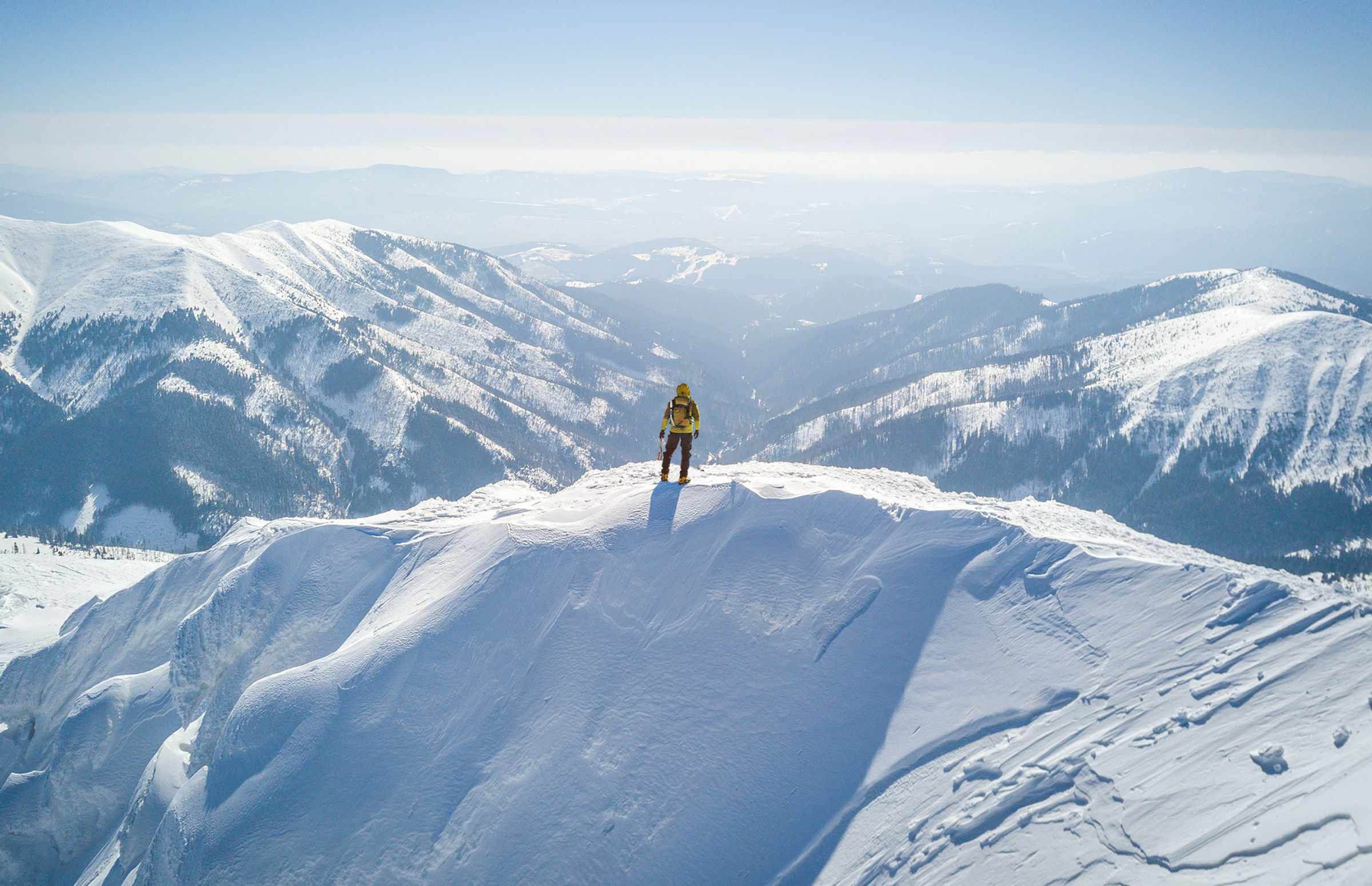 A climber standing on a snowy summit looking out over a mountain range
